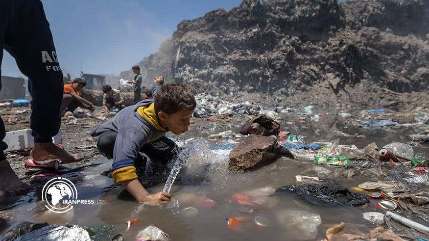 Iranpress: العطش يدفع طفلاً للشرب من مياه ملوثة وسط أكوام النفايات في غزة